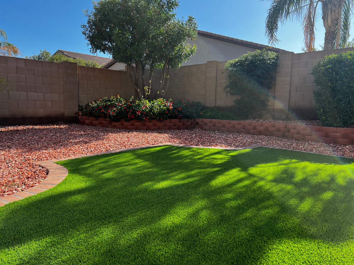 Artificial grass and a raised planter with trimmed bushes and a tree.